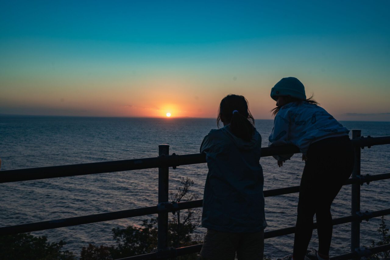 世界自然遺産・知床でオホーツク海に沈む夕日を見る小学生と中学生